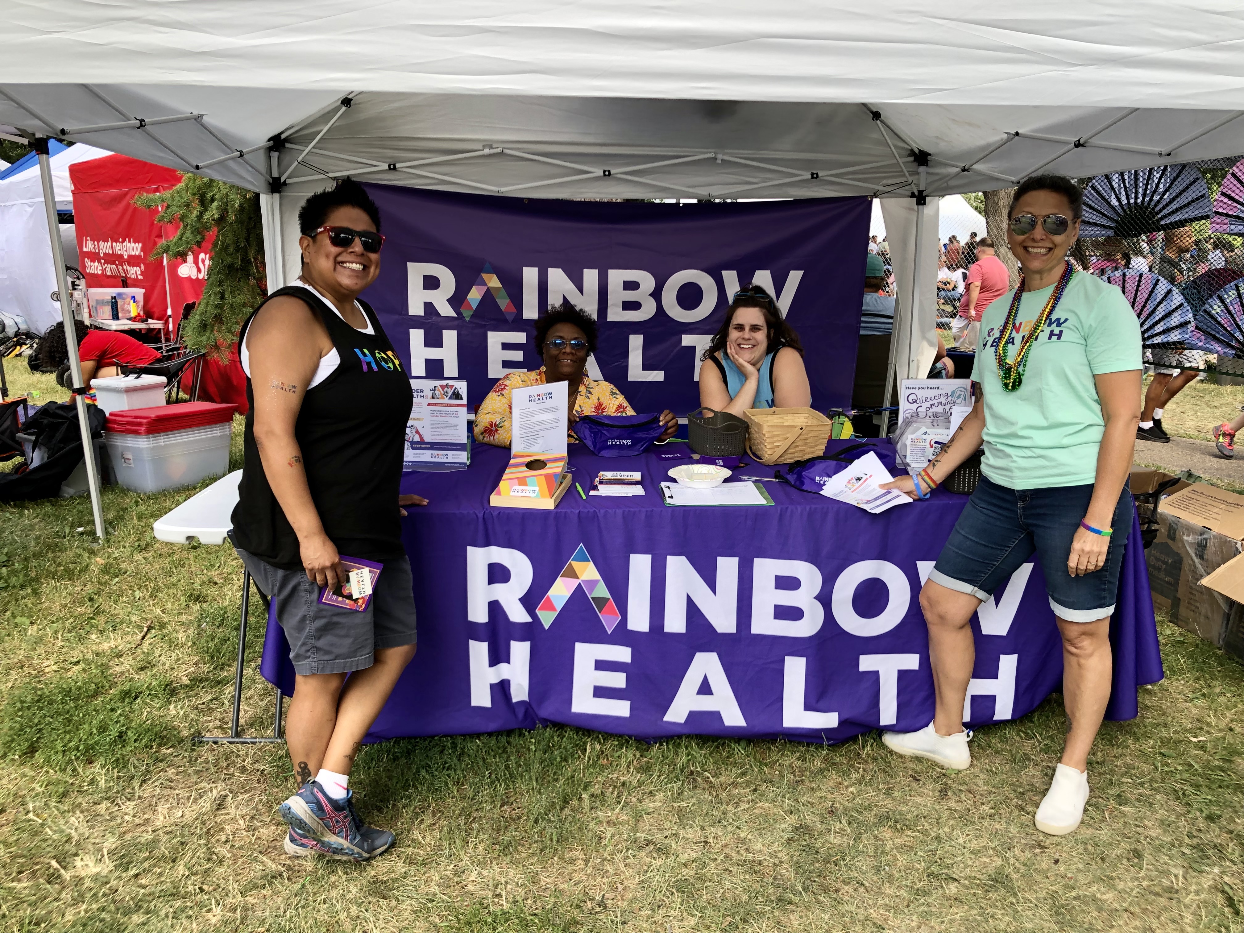 [Picture 2] Rainbow Health staff and volunteers in the booth at the 2022 Twin Cities Pride Festival. Over 500 people visited our booth where they were greeted with an opportunity to win raffle prizes, fun swag items, glitter and skin care kits donated by L’Oreal!